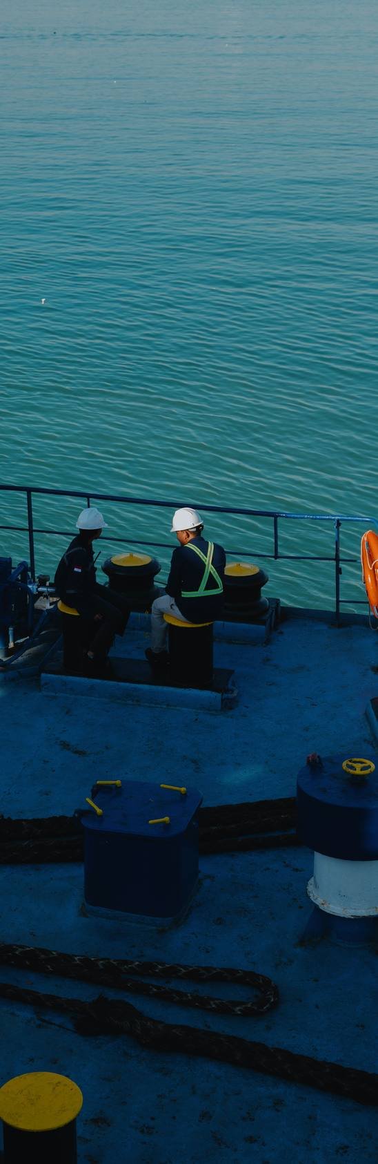 Crew members wearing helmets talking by the railing of a vessel at the dock